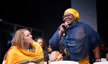 a woman standing in an audience smiles while holding a microphone